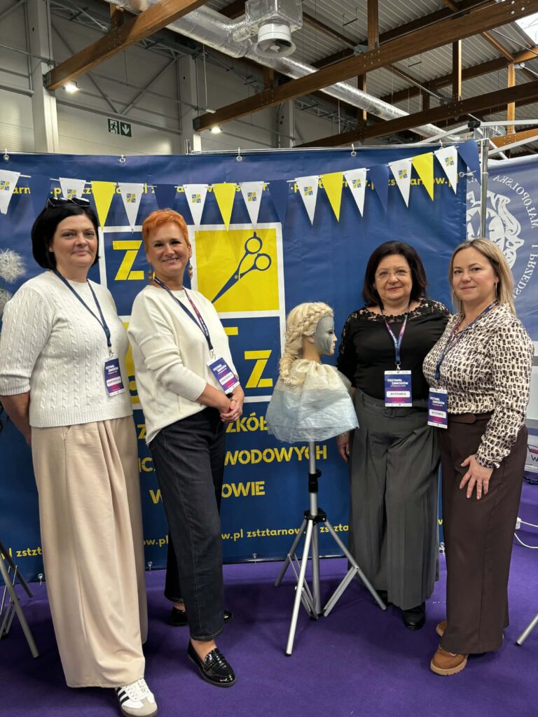 Kadra szkoły pozuje na tle banneru szkoły. Pani dyrektor i trzy nauczycielki