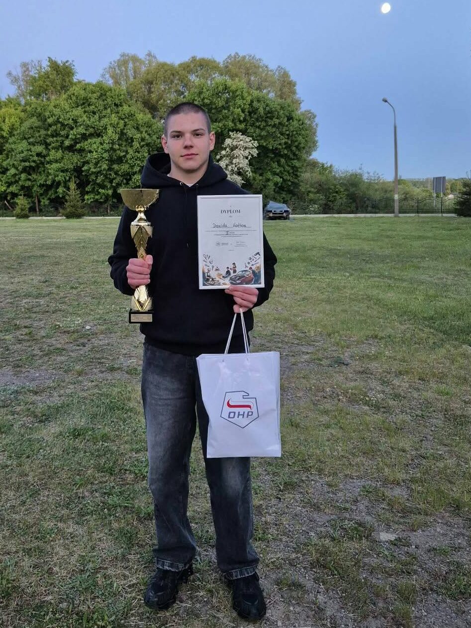 Uczeń z pucharem, dyplomem i nagrodą stojący na tle drzew